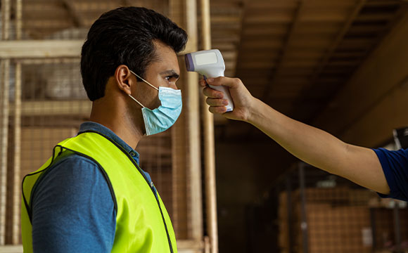 Male in a green vest with a surgical mask on getting his temperature checked