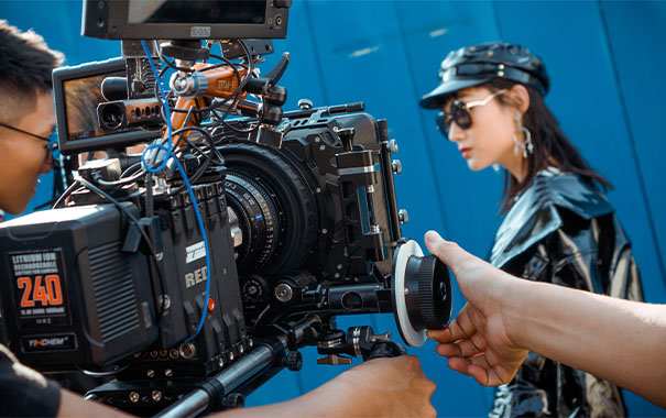 two indivudals operating a movie grade camera that is filming a young fashionable female