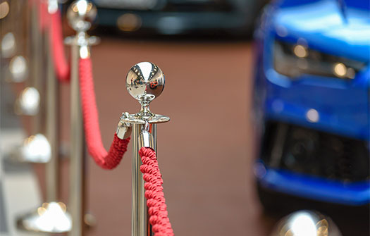 Red carpet ropes with gold posts and blue luxury car in the background