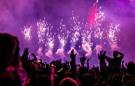 view from the crowd of a concert with purple lighting, fireworks, and smoke